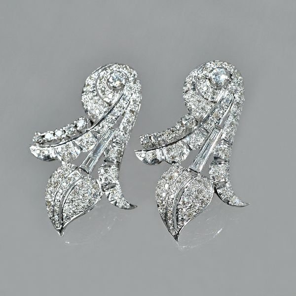 A pair of diamond set earrings of stylized scrolling leaf design, set throughout with baguette and circular cut diamonds, set in white precious metal,