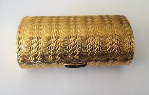 A Kutchinsky London 9ct gold cigarette case, of oval form, the exterior engine turned and with a sapphire set thumbpiece, mounted with a row of five c