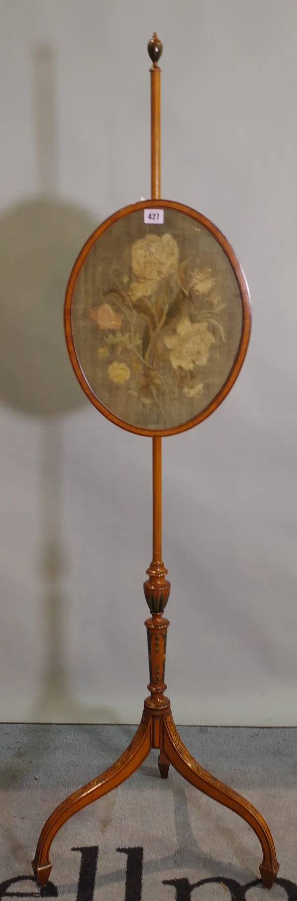 An Edwardian satinwood and polychrome painted polescreen with oval framed needlework of flowers on three outswept supports, 31cm wide x 146cm high.