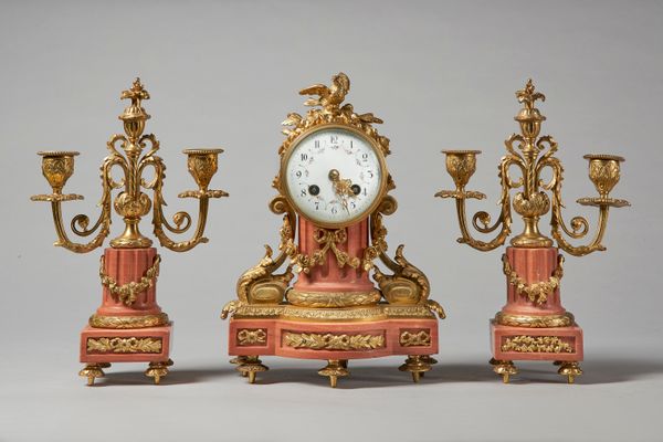 A French giltbrass and pink marble garnitureIn the Louis XVI style, circa 1910Comprising a mantel clock and a pair of twin-light candelabra, the clock