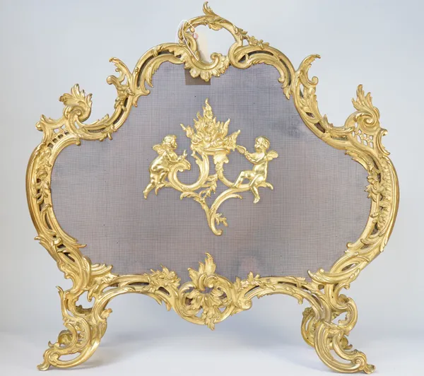 A rococo style gilt metal and wire mesh fire screen of foliate scroll design, early 20th century centred with two Cupid figures fanning a fire, 71cm h