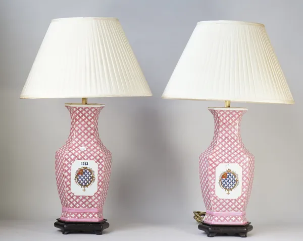 A pair of modern Chinese style porcelain table lamps, pink ground with central armorial decoration, on wooden stands with cream pleated shades, 40cm h