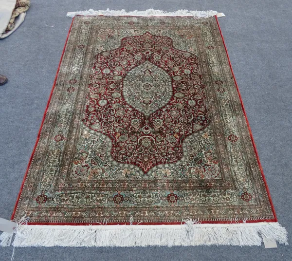 A silk Hereke rug, Turkish, the madder field with pale medallion and spandrels, all with intricate floral sprays and palmette, a pale indigo cartouche