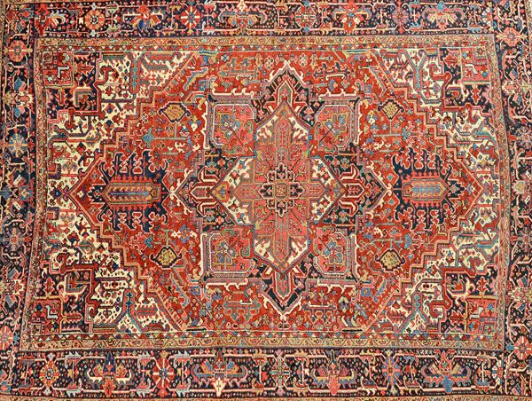 An Heriz carpet, Persian, the madder field with a bold medallion, matching spandrels, all with angular floral sprays, a black palmette rosette and lea