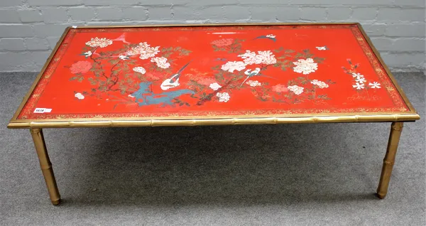 A Chinese red lacquer panel topped low table, with painted floral decoration on simulated bamboo brass frame base, 120cm wide x 62cm high.