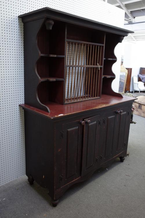 A distressed red and black painted pine dresser, the enclosed shelf back with fitted plate rack over four raised panel doors, on bun feet, 157cm wide