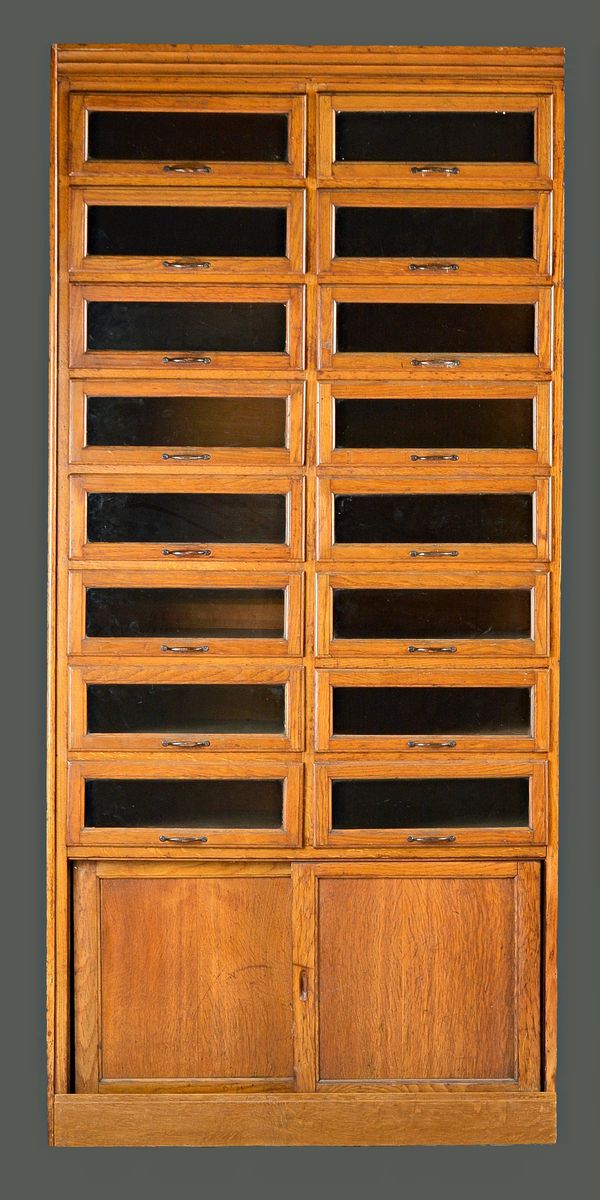 A mid-20th century oak haberdashery cabinet with two rows of eight glass fronted drawers over sliding cupboards, 90cm wide x 194cm high.