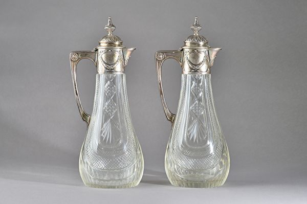 A copy of a pair of Faberge faceted glass claret jugs, each body of swept oval form, with facet cut decoration, the mounts decorated with foliate swag