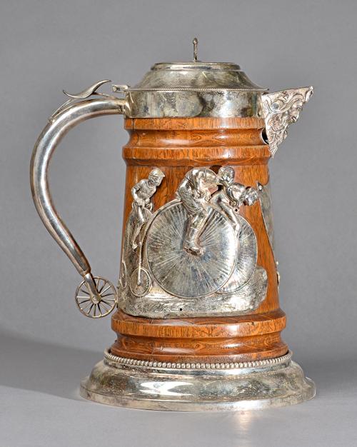 A silver plated metal mounted oak large hinge lidded flagon, the body decorated with cyclists, raised on a circular base, having a beaded rim, the han