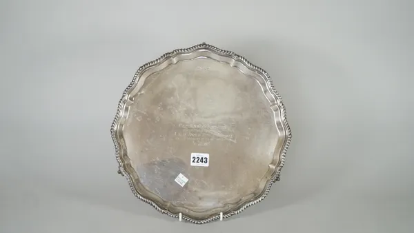 A silver salver, having a shaped rim, decorated with a gadrooned border, presentation inscribed to the centre, raised on three ball and claw feet, She