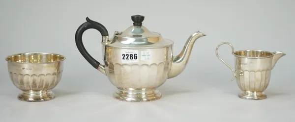 A silver three piece tea set, comprising; a teapot,having black fittings, a sugar bowl and a milk jug, each piece of panelled circular form and with a