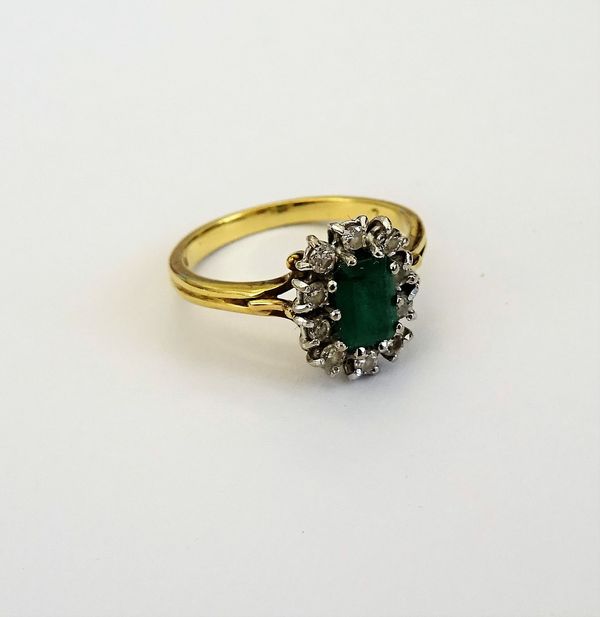 An 18ct gold, emerald and diamond cluster ring, claw set with the rectangular step cut emerald at the centre, in a surround of ten circular cut diamon