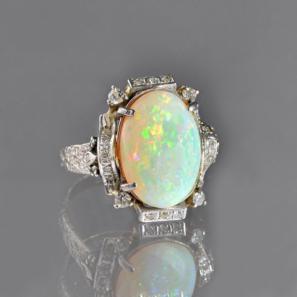 An opal and diamond ring, claw set with the oval opal at the centre and with circular cut diamonds mounted to the surround, the shank with a textured