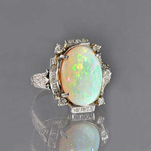 An opal and diamond ring, claw set with the oval opal at the centre and with circular cut diamonds mounted to the surround, the shank with a textured