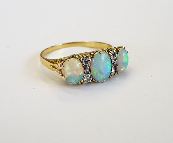 A gold ring, mounted with three oval opals and with two rows of three small cushion shaped diamonds mounted at intervals, the mount decorated with scr