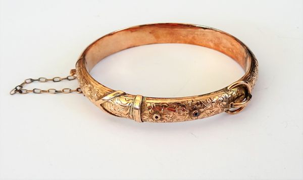 A 9ct gold oval hinged bangle, with foliate engraved decoration, on a snap clasp, fitted with a safety chain, Birmingham 1907, gross weight 11.2 gms.