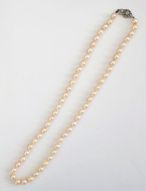 A single row necklace of uniform cultured pearls, on a diamond set clasp, pierced in an openwork design, length including clasp 47.5cm, with a case.