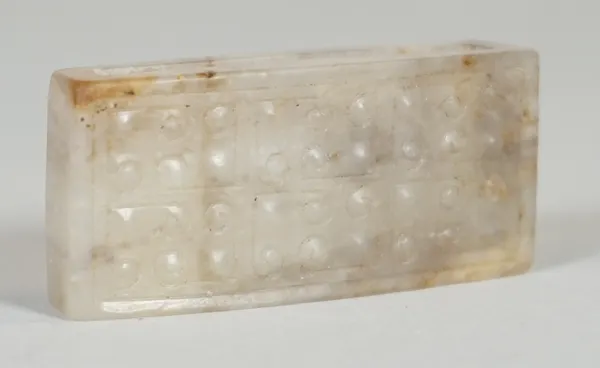 A Chinese jade rectangular sword slide, possibly Han dynasty, the upper surface carved with a `grain' pattern, the stone of greyish tone with russet i