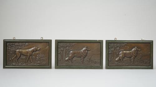 Three rectangular bronze plaques, early 20th century, each relief cast with a dog against a landscape within a verdigris patinated framed border, sign