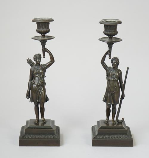A pair of 19th century bronze figural candlesticks; Diana the huntress and one other, both supporting a circular, foliate cast sconce on a stepped squ