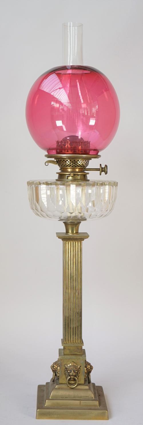 A Victorian brass oil lamp of square fluted column form with a clear cut glass reservoir, Hinks Duplex burner and a cranberry glass shade of globular