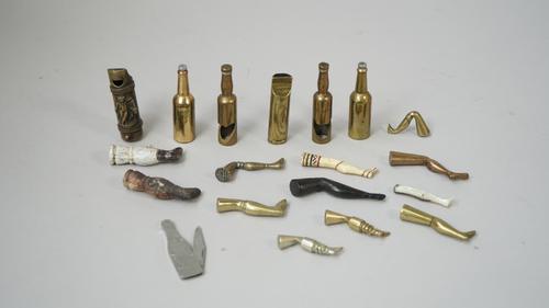 A collection of pipe tampers, early 20th century, modelled and cast as a leg in brass, porcelain and bone, also a brass whistle/vesta, a 'Dry Monopole