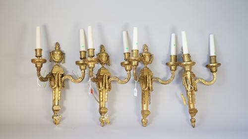 A set of four Louis XVI style ormolu twin light wall appliques, early 20th century, each cast with flaming urn finials over a tapering square form bac
