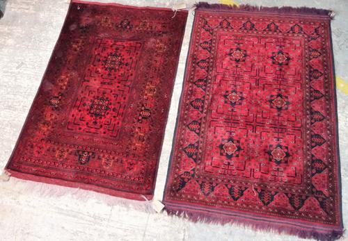 Two similar Afghan Beluche rugs, each with madder fields, one with two square sections, 150cm x 100cm, the other with six sections, each with a plant