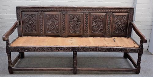 A 17th century and later oak settle with carved frieze panel back on turned supports, 183cm wide x 87cm high.