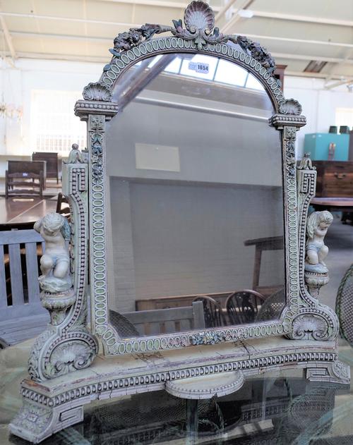 An early 20th century polychrome painted gesso swing frame toilet mirror, relief moulded with flowers and shells on putto mounted supports, 85cm wide