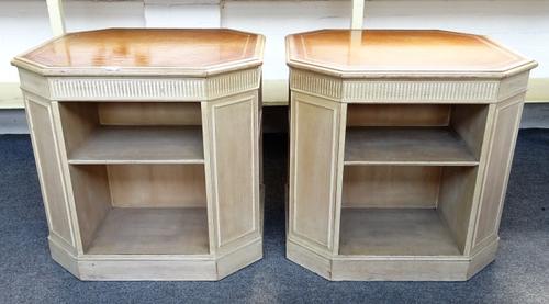 A pair of grey painted pine book stands of canted square form, each with gilt tooled leather inset tops above opposing open shelves, 70cm wide x 65cm
