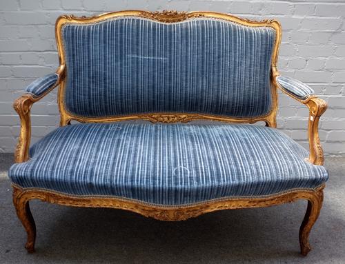 A Louis XV style gilt framed open arm sofa with floral carved crest and serpentine seat on cabriole supports, 127cm wide x 95cm high.