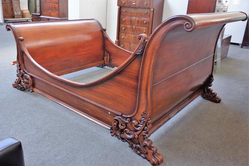 A hardwood sleigh bed, each scroll end with carved rococo revival decoration, on lions paw feet, united by concave side rails, 194cm wide x 140cm high