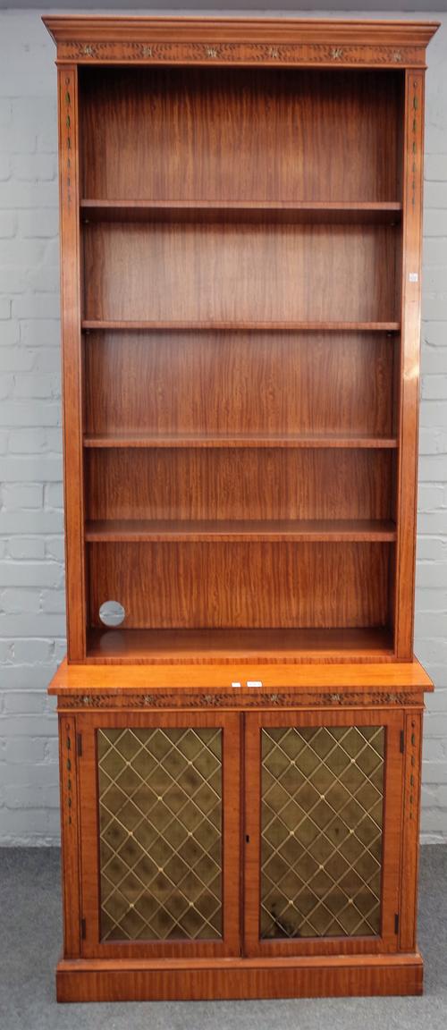A 20th century floral polychrome painted satinwood bookcase/ cabinet, the open four tier shelf back over a pair of brass grille cupboards, 89cm wide x