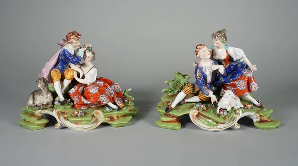 A pair of German porcelain figure groups, 20th century, each modelled as an embracing young couple seated with a lamb or goat, blue painted mark, each