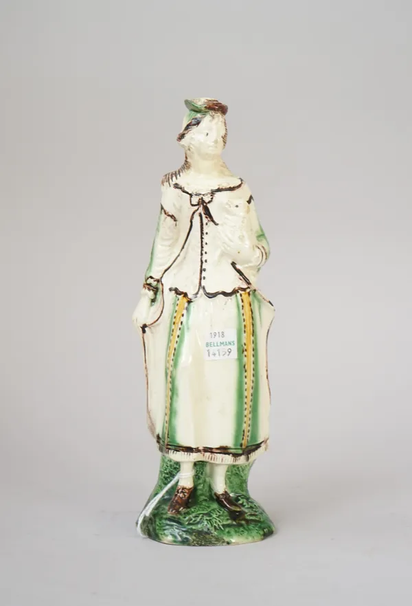 A rare creamware figure of a shepherdess, circa 1780, modelled standing holding a lamb under her left arm, wearing a hat, cape and dress picked out in