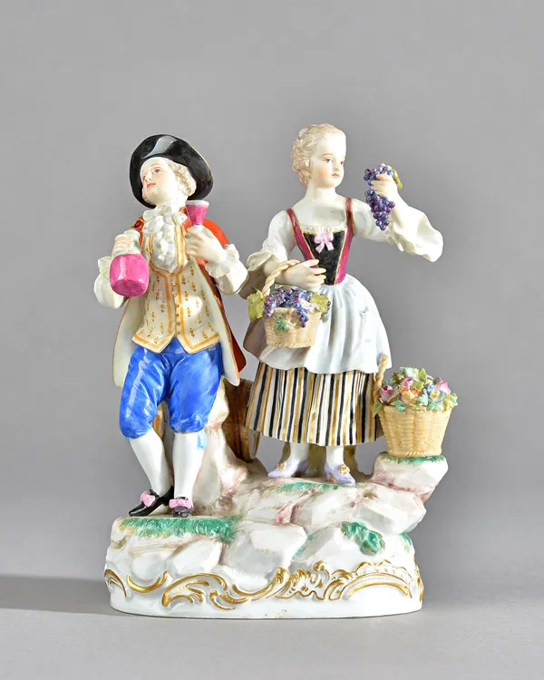 A Meissen group of vintners, circa 1900, modelled as a youth and companion standing on a rocky mound base, he holding a flask and glass, she carrying