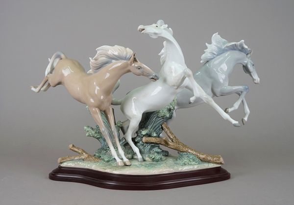 A Lladro porcelain equestrian group 'Born Free' depicting three frolicking horses atop a naturalistic shaped base and wooden plinth, 41cm high overall