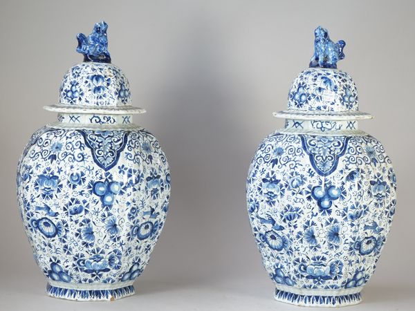 A pair of Dutch Delft blue and white ribbed oviform vases, 19th century, painted with birds amongst flowers and fruit, the covers with lion dog knops,