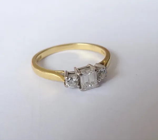 An 18ct gold and diamond three stone ring, claw set with the principal cut cornered rectangular emerald cut diamond to the centre, between two smaller