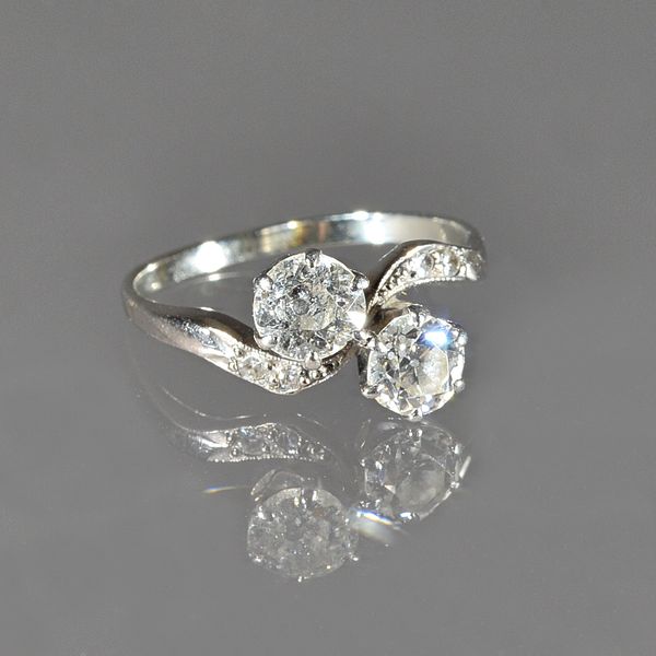 A diamond two stone ring, claw set with the two principal cushion shaped diamonds to the centre, in a twistover design between diamond two stone shoul