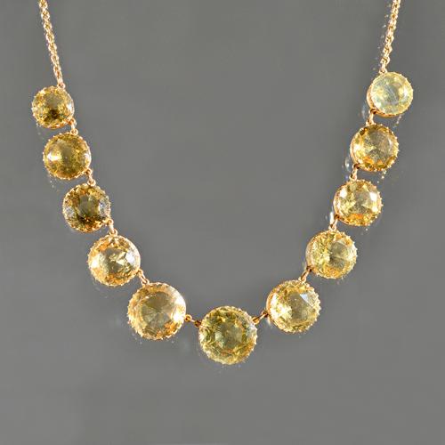 A gold and citrine necklace, the front claw set with a row of eleven circular cut citrines graduating in size to the centre stone, on an oval link cha