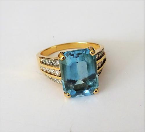 A gold, blue topaz and diamond ring, claw set with the cut cornered rectangular blue topaz to the centre, the shoulders mounted with three rows of tap