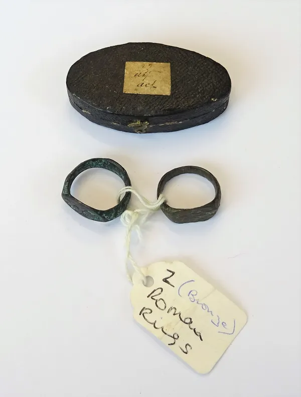 Two Ancient bronze signet style intaglio rings, possibly Roman, with a later oval case, (2).