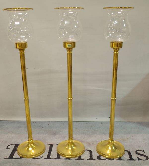 A set of three 20th century brass and glass standing hurricane lamps, 119cm high.   Provenance; property from the late Sir David Tang    This lot has