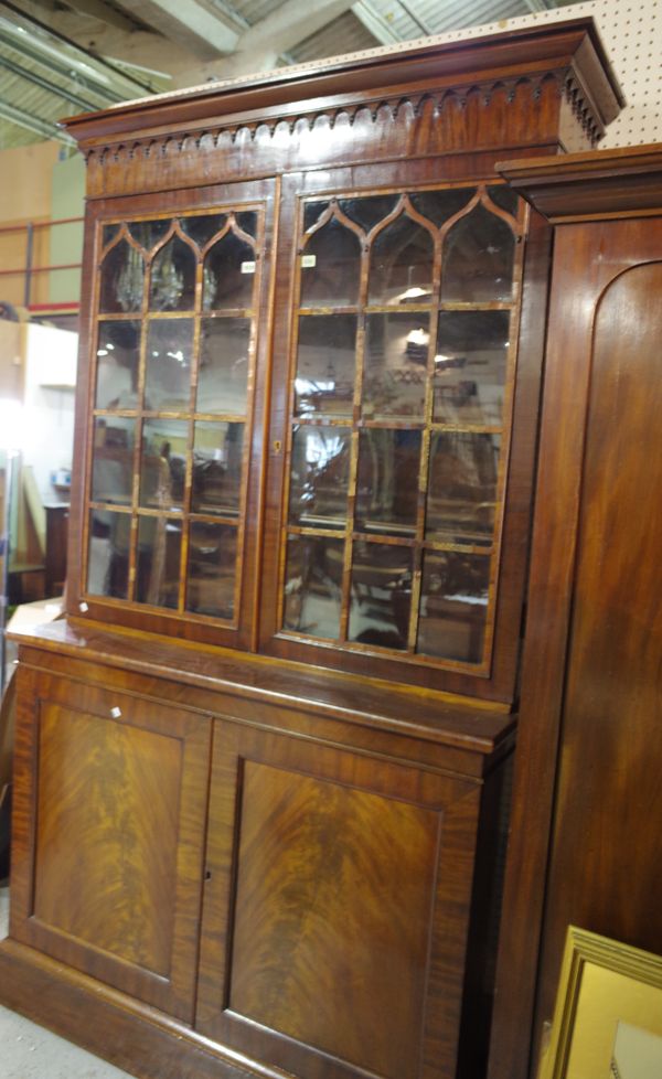 A mahogany library bookcase, Regency top on associated base, with Gothic arched frieze above two glazed doors and two cupboard doors on a plinth base,