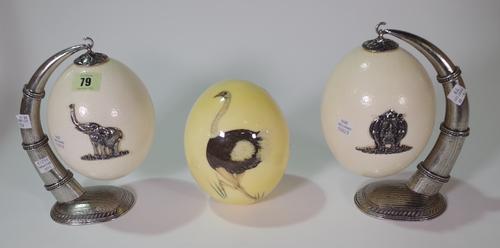 A pair of late 19th early 20th century white metal mounted ostrich eggs on hanging stands and a painted ostrich egg, 16cm high (3). CAB