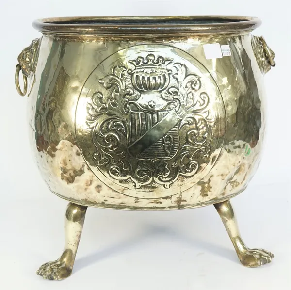 A Victorian polished brass log bin of circular form, flanked by lion ring handles on three lion paw feet, with embossed heraldic crest to the centre,