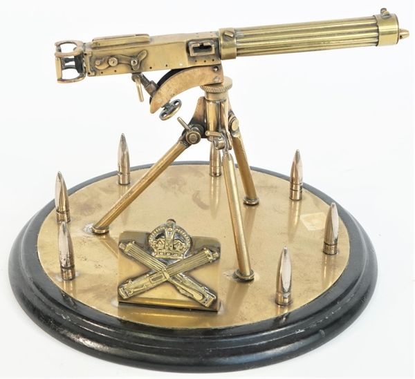 A brass model of a WWI Vickers machine gun, 20th century, on a tripod and circular base within a border of upturned bullets on an ebonised circular ba