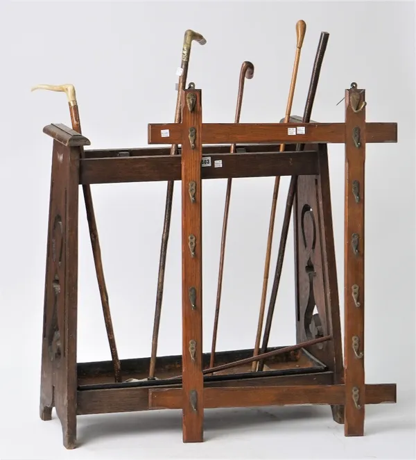 An early 20th century oak stick stand of Arts and Crafts style, 74cm high, containing five walking sticks and two leather bound riding whips, and a la